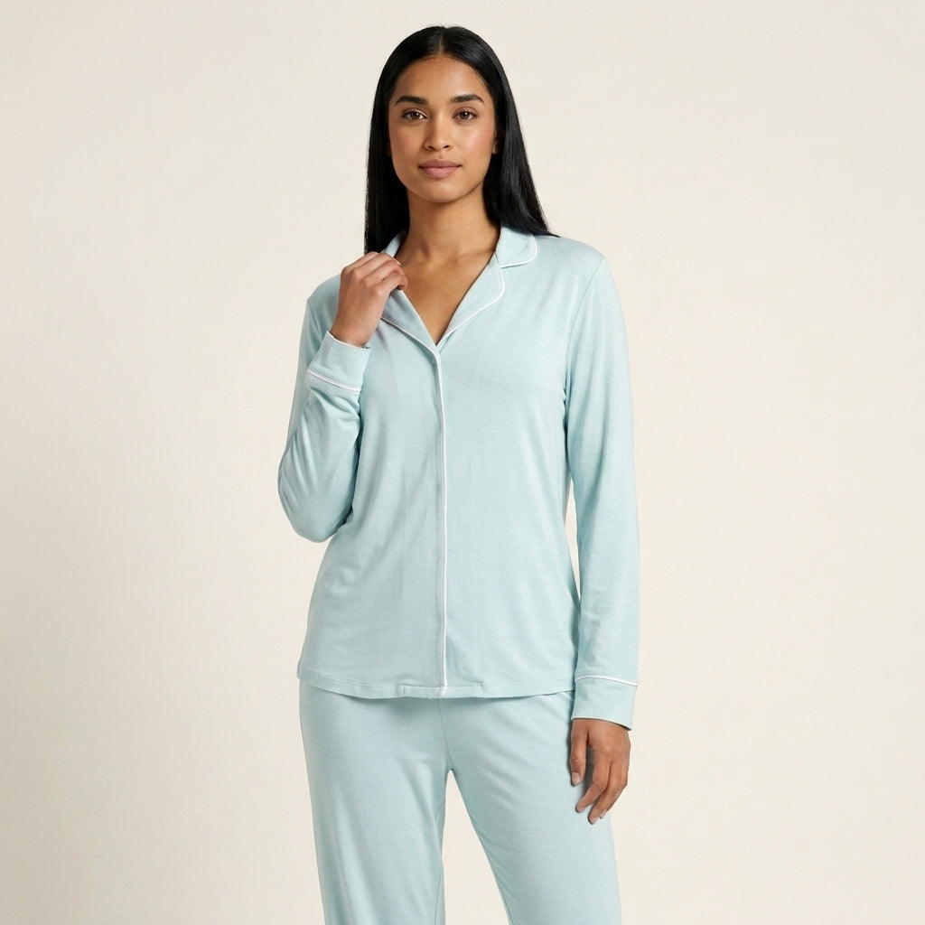 A woman modeling a light blue long-sleeve pajama set with a collared button-front top and matching pants against a plain beige studio background. Available in Ice Mint XS, Ice Mint S, Ice Mint M, Ice Mint L