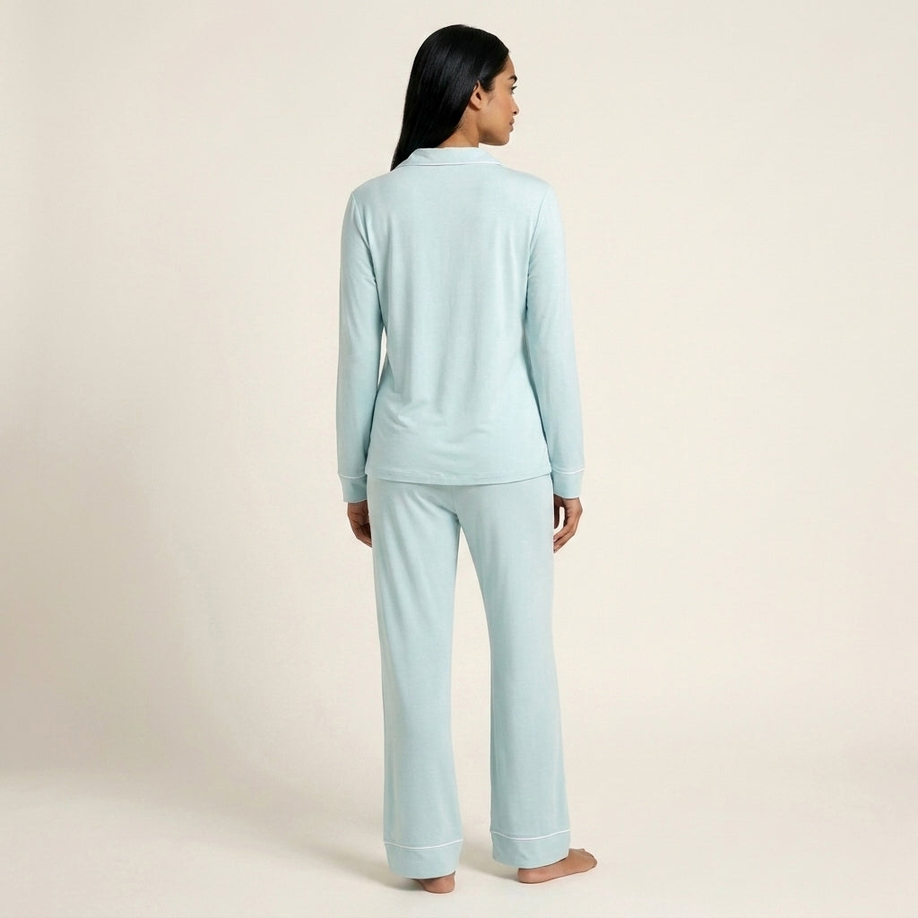 A woman wearing a light blue long-sleeve pajama set, viewed from the back, standing against a plain beige studio background. Available in Ice Mint XS, Ice Mint S, Ice Mint M, Ice Mint L