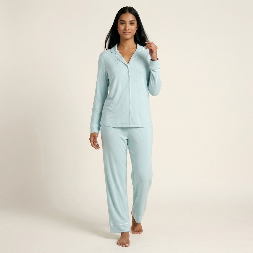 A woman modeling a light blue two-piece pajama set consisting of a long-sleeve button-front top and matching pants, photographed against a plain light beige studio background. Available in Ice Mint XS, Ice Mint S, Ice Mint M, Ice Mint L