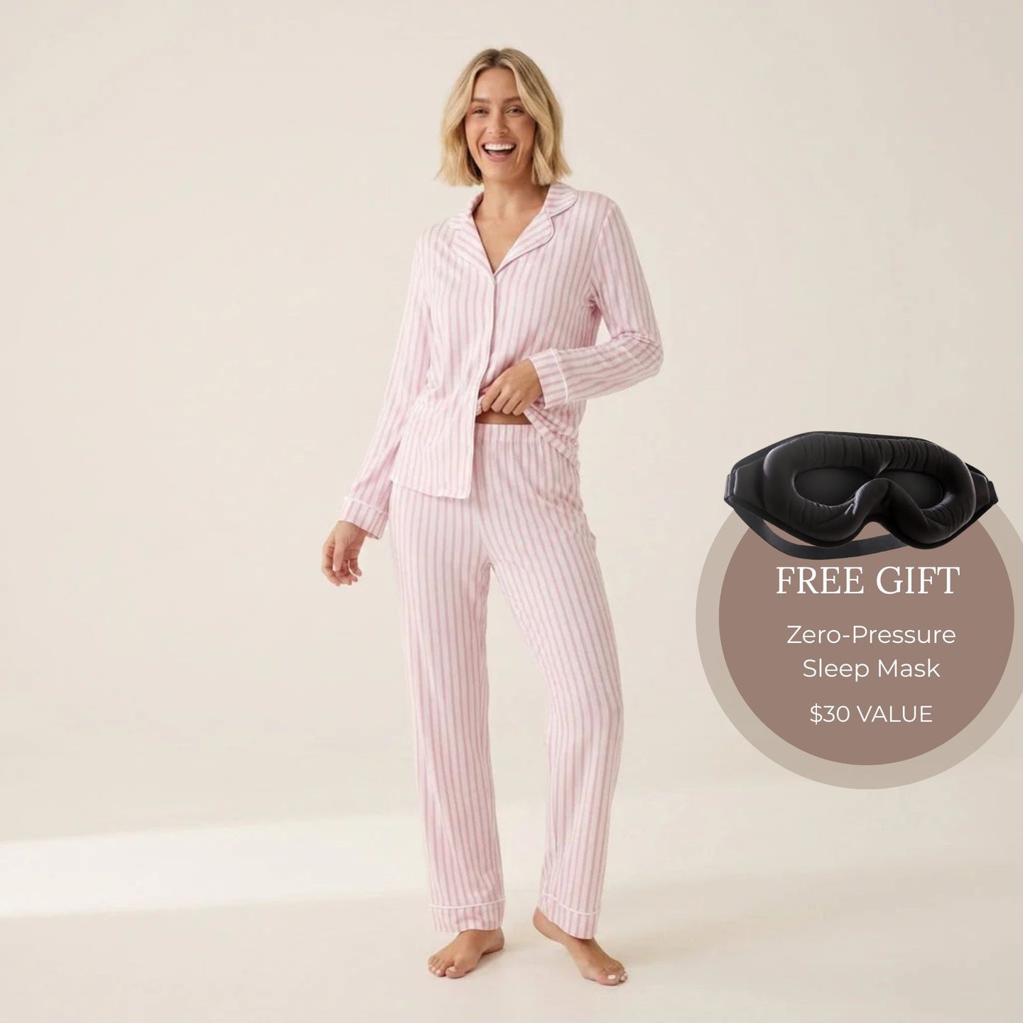 A woman modeling a two-piece pink and white vertically striped pajama set, consisting of a long-sleeve button-up shirt and matching pants, against a plain beige studio background. Available in Pink Pinstripe XS, Pink Pinstripe S, Pink Pinstripe M, Pink Pinstripe L