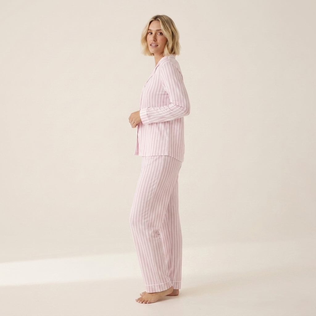 A woman modeling a two-piece pajama set with light pink and white vertical stripes, standing against a plain off-white studio background. Available in Pink Pinstripe XS, Pink Pinstripe S, Pink Pinstripe M, Pink Pinstripe L
