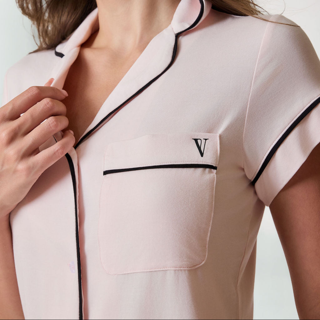 Woman wearing pajama set with black trim on a white background. Available in Blush Pink XS, Blush Pink S, Blush Pink M, Blush Pink L